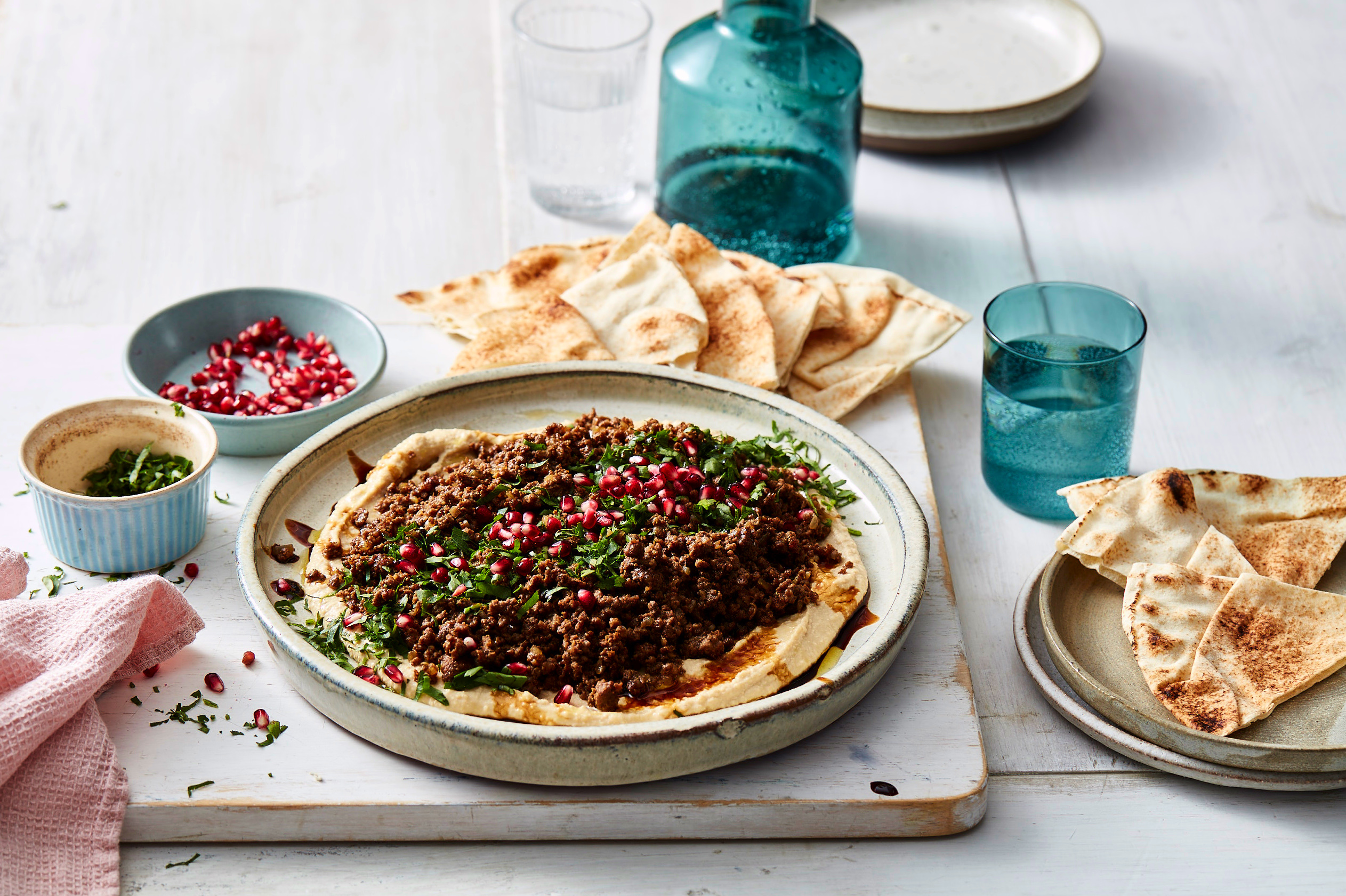 Close up of completed hummus with spiced lamb dish with pita crisps on the side