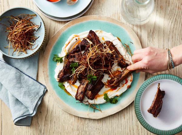 Chef's hand spooning chilli oil over plated ribs from a birds eye view.